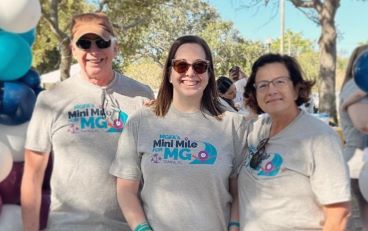 Three people stand underneath a balloon arch wearing Mini Mile for MG tshirts
