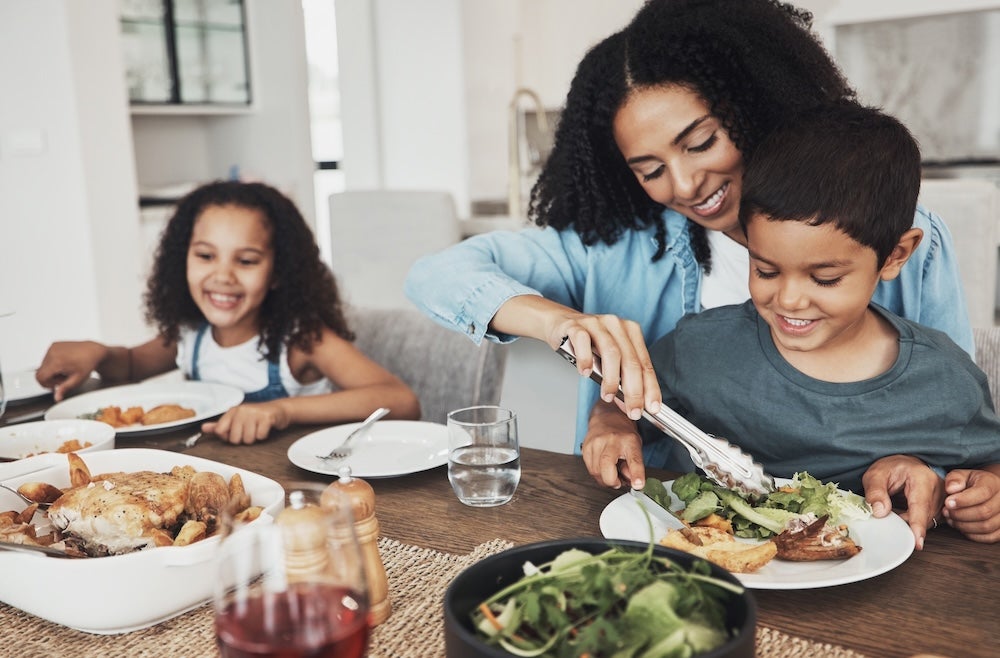 Mother using tongs to serve a meal to her two grade-school children